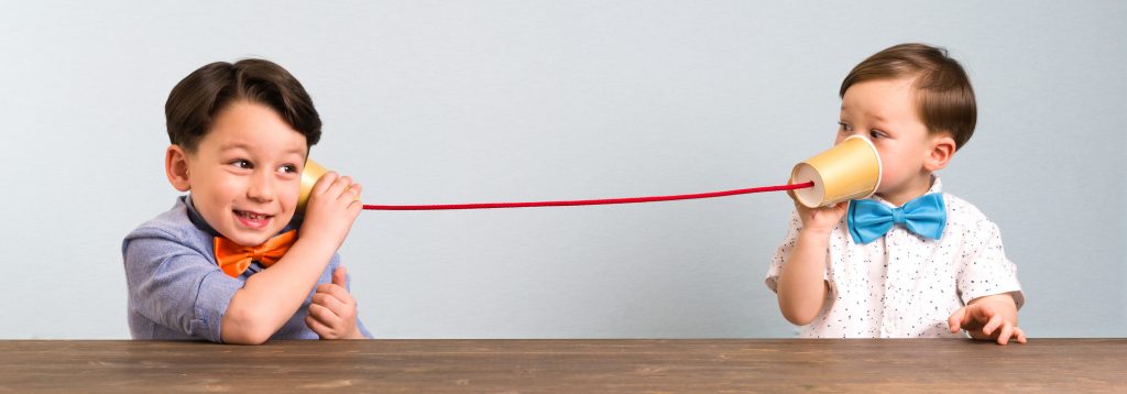 Two childeren are using paper cups as a telephone